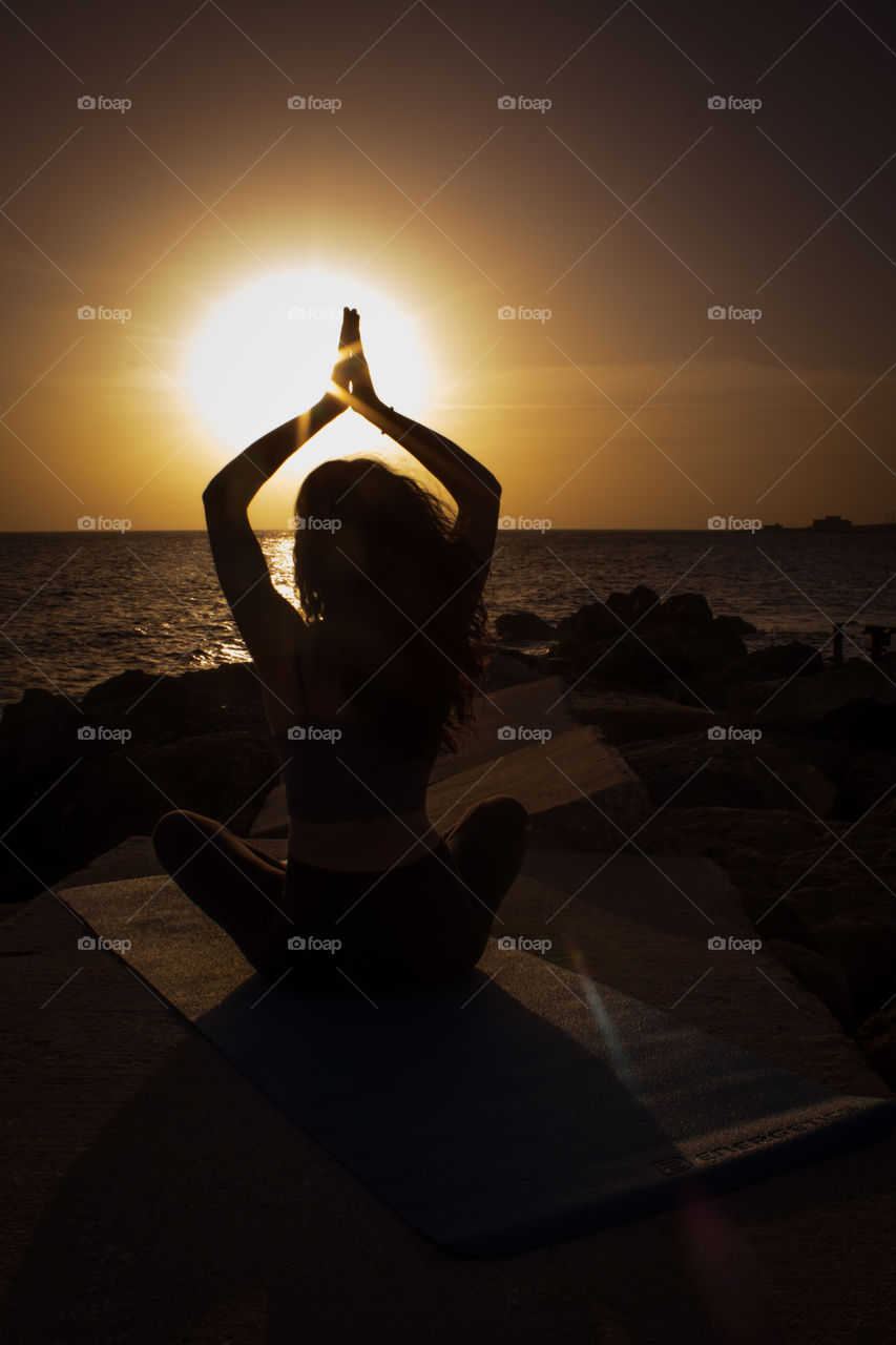 Woman meditating in a prayer position at beach during sunset