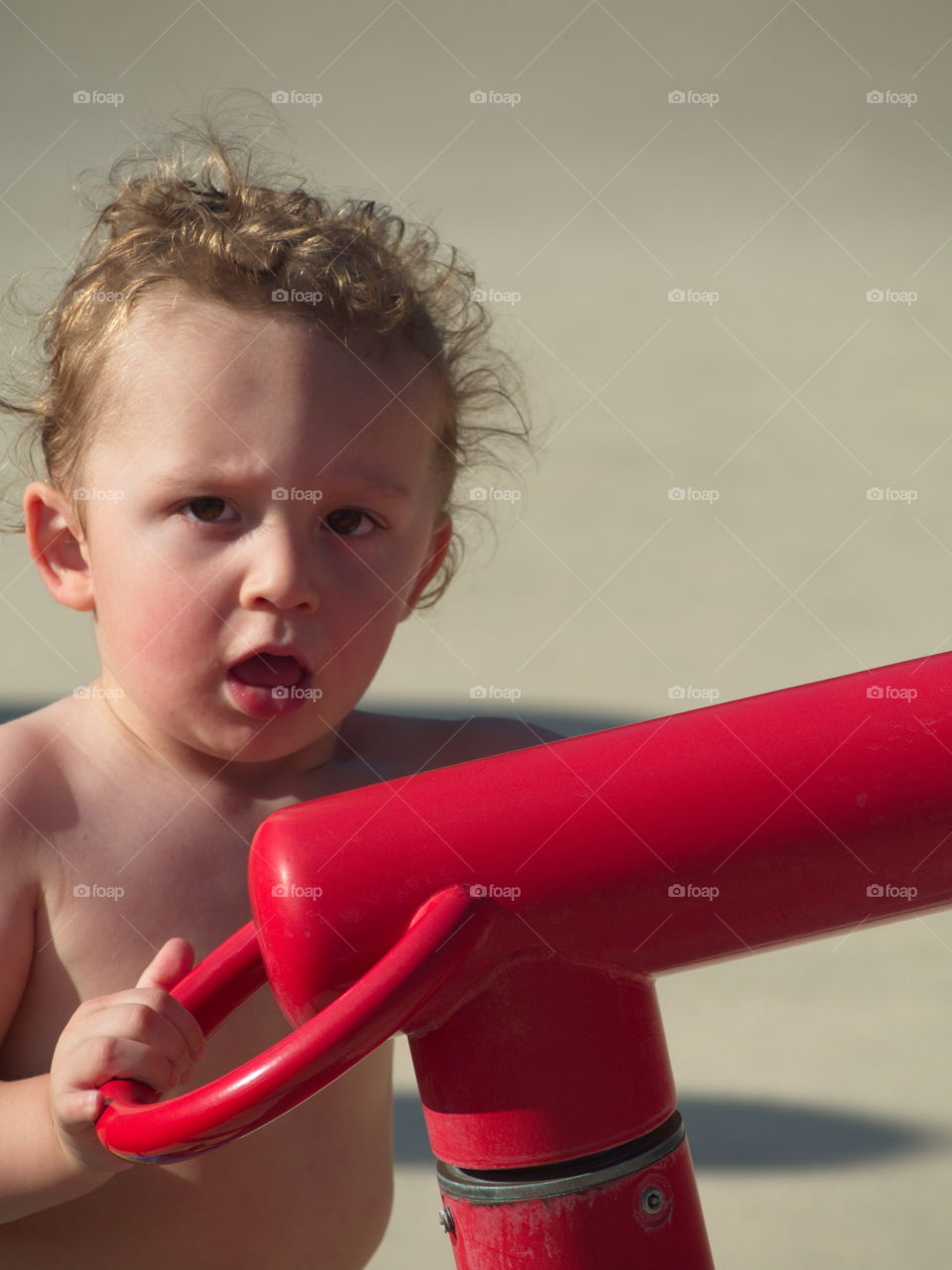 A cute little boy playing with a water toy at an outdoor swimming pool on a sunny summer day. 