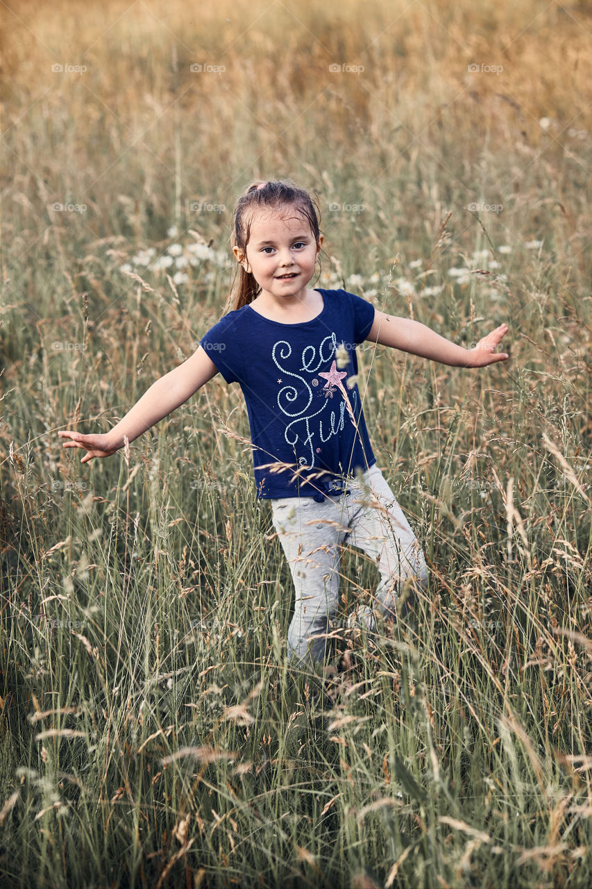 Little happy kid playing in a tall grass in the countryside. Candid people, real moments, authentic situations