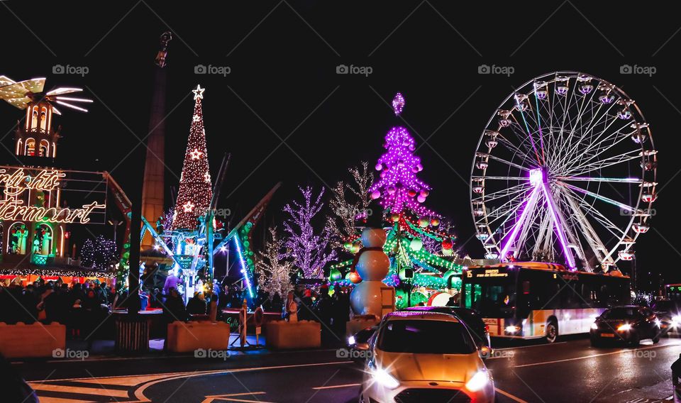 Beautiful view of Luxembourg city at night with colorful Christmas installations, Christmas tree, Ferris wheel and cars driving on the road, close-up side view.