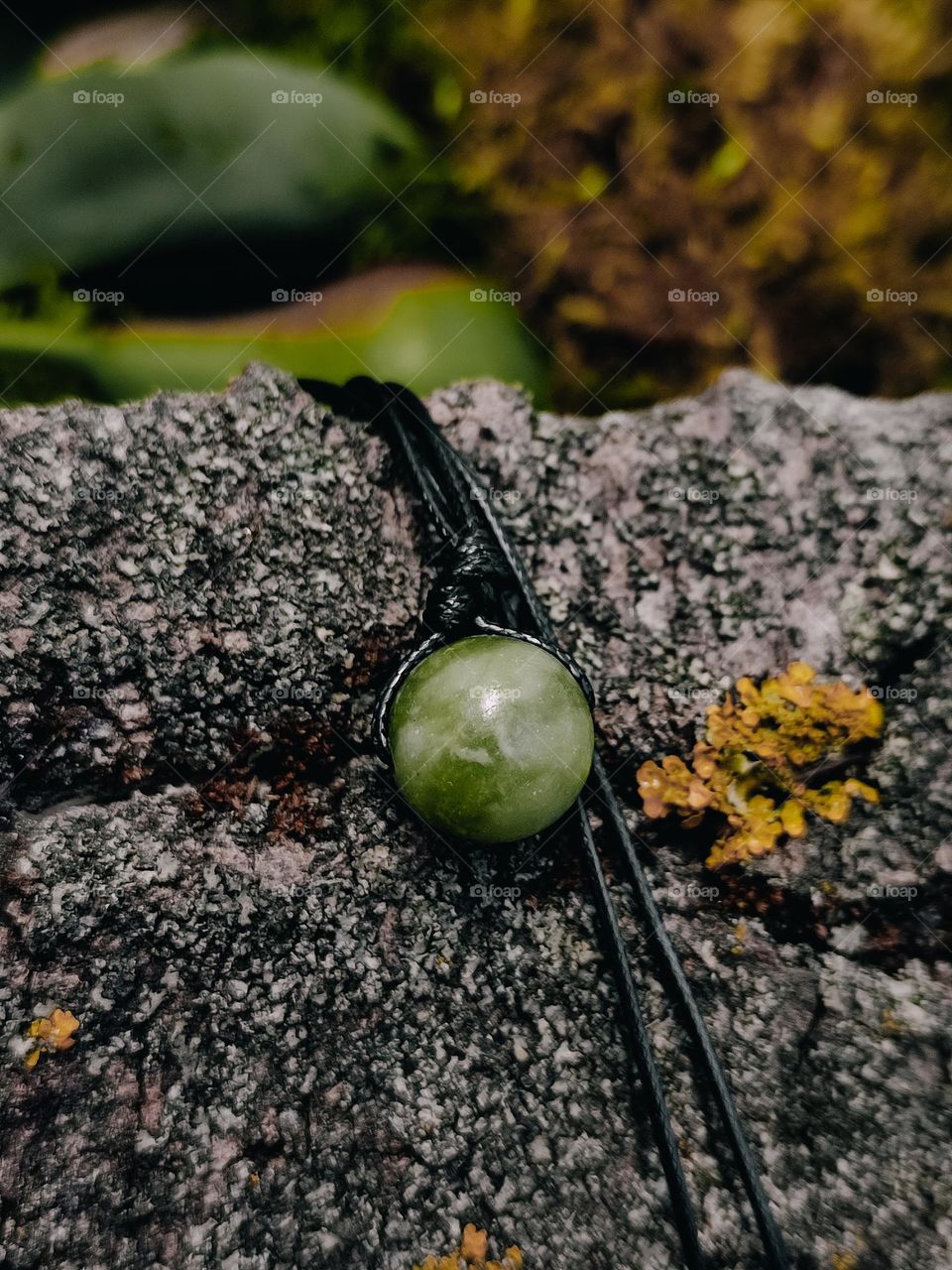Green nephritis round beaded chocker on black cord, wooden texture surface macro, jewelry