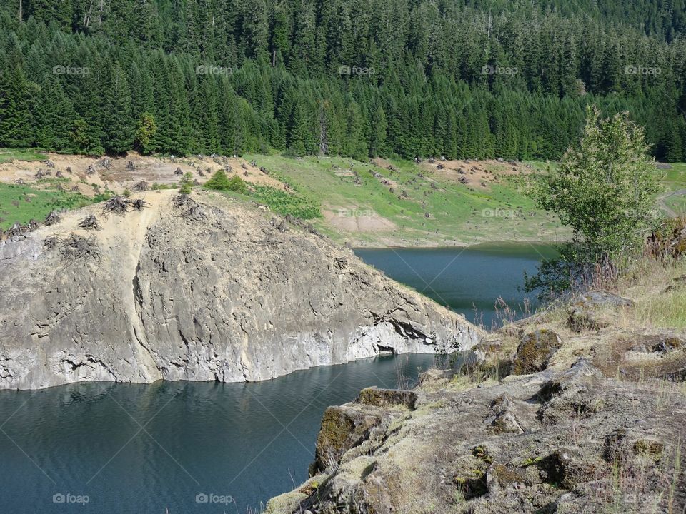 The steep, rocky, and tree covered shores of Cougar Reservoir in Western Oregon on a sunny day. 