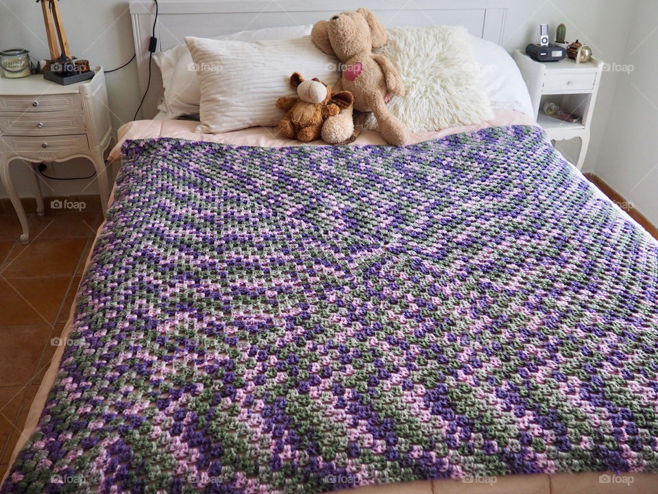 Shades of purple hand made crochet blanket on girl’s bed.