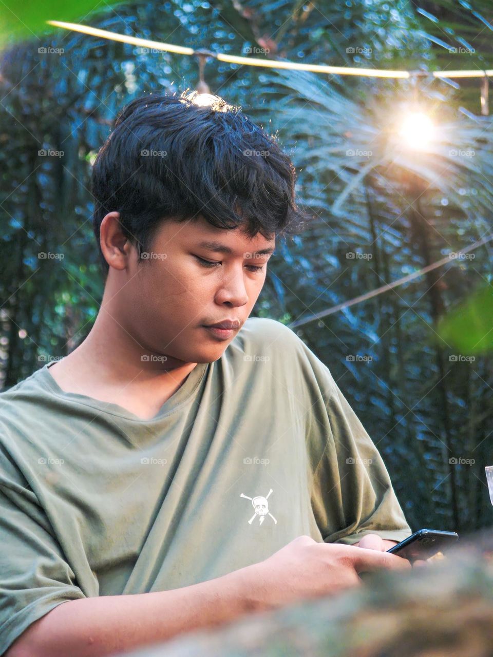 Close-up of a young man sitting looking at a cell phone in the forest