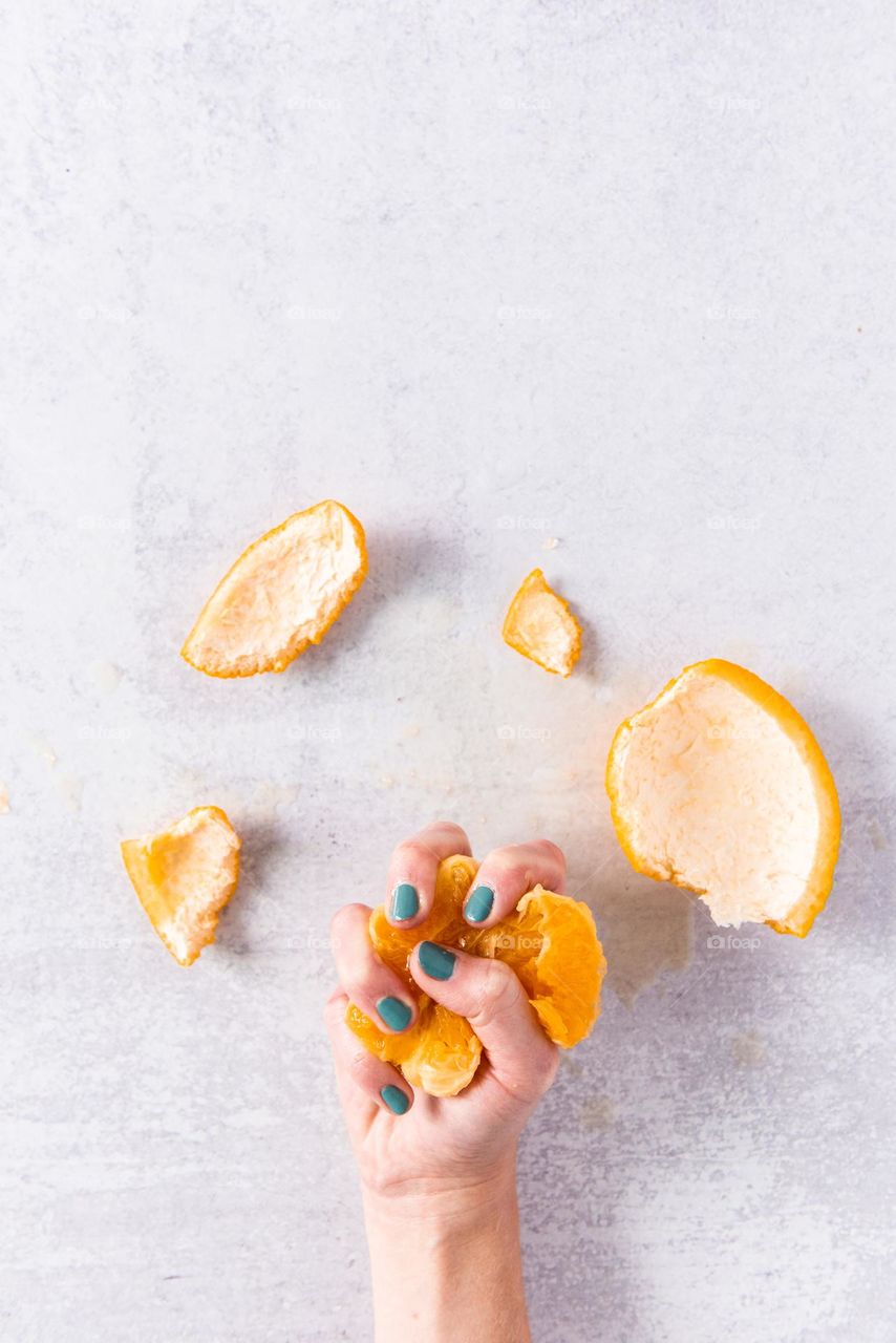 Woman’s hand with painted nails squeezing an orange fruit 