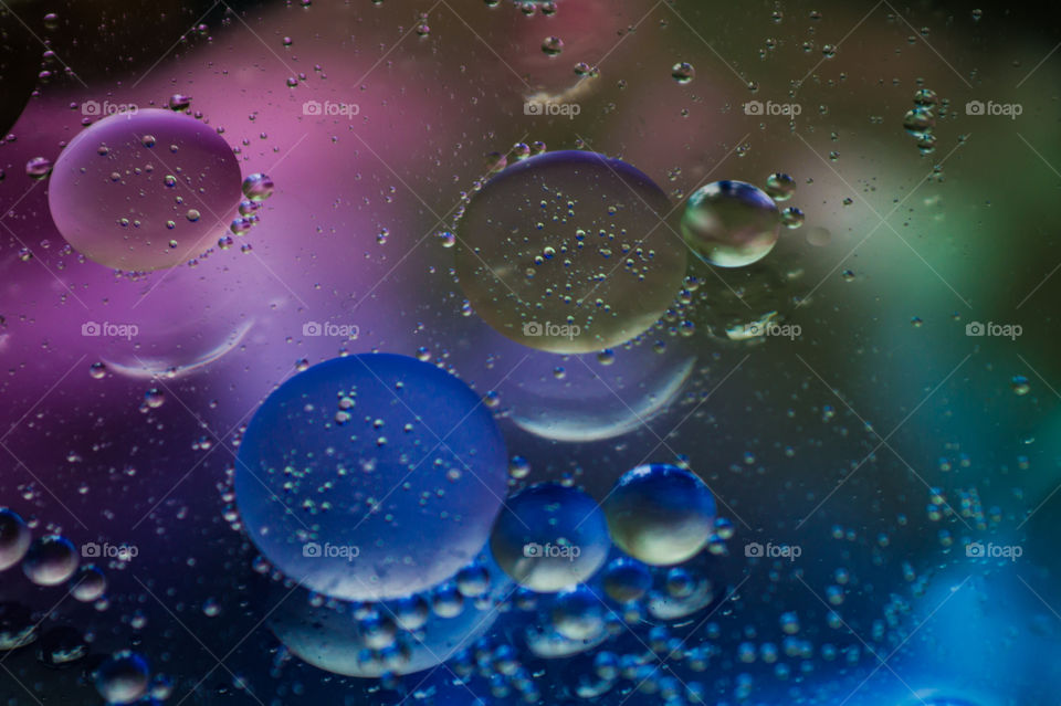 Bubbles of vegetable oil in clear water on a glass and transparent lid from a frying pan on colored paper.