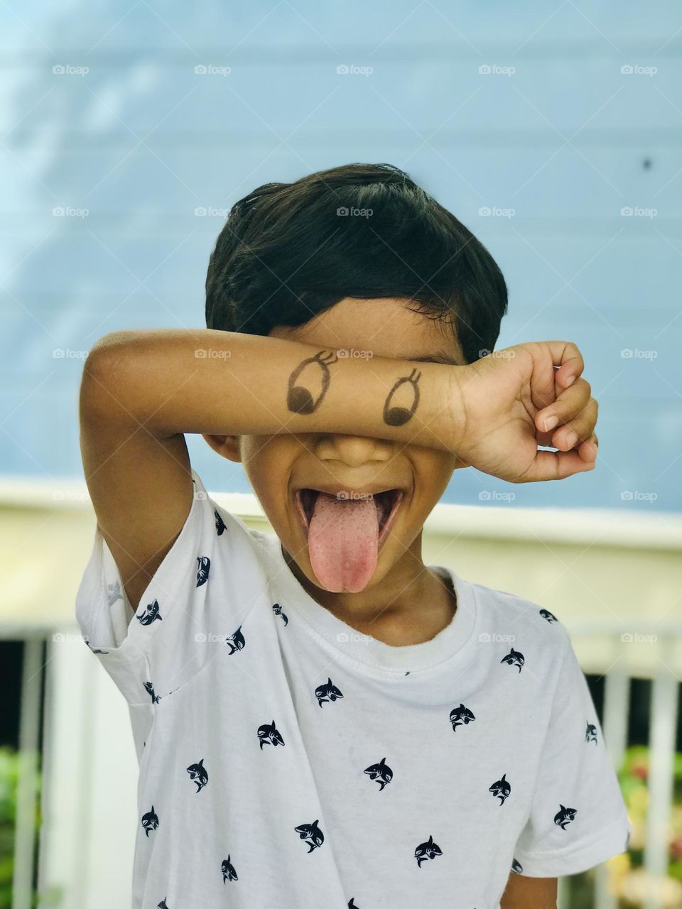 Fun with kids.a boy close his eyes with cartoon eyes draw on his hand and keep his tongue out and making fun.