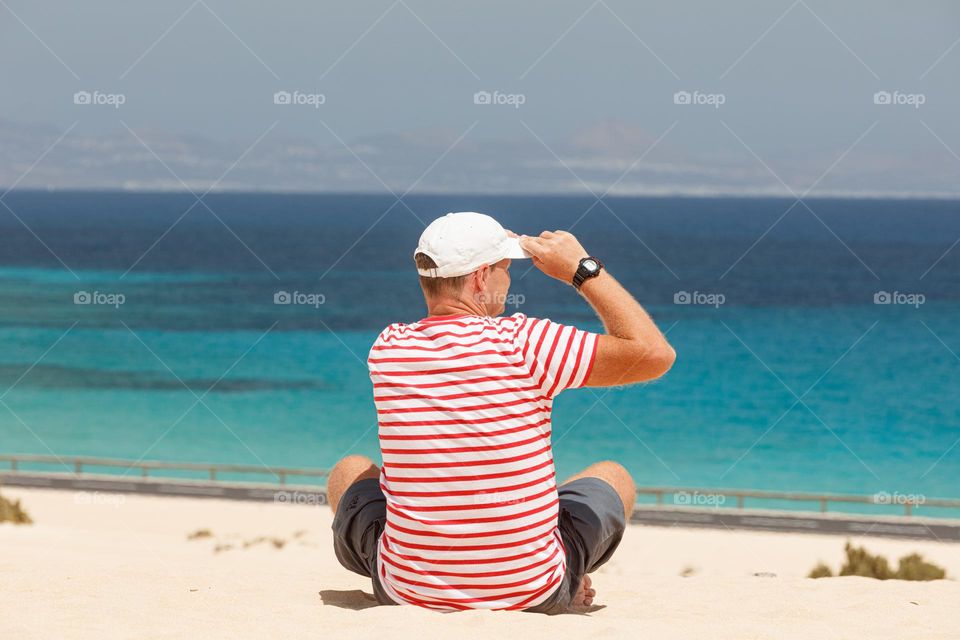 man admiring the view of the ocean cost sitting on the sandy beach