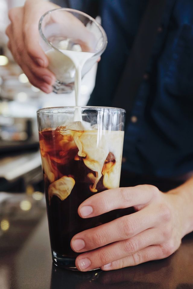 Person's hand pouring milk over iced coffee