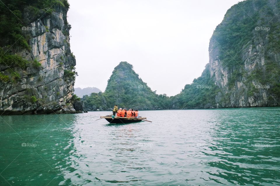 A boat is carrying tourists in the bay,cool blue waters and gray mountains a lot of trees grow