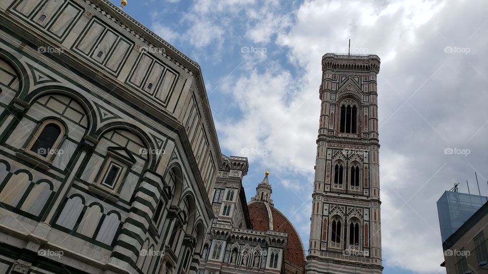 Unique view of the Baptistery of Saint John, and the Florence Cathedral roof, and the tall Giotto's Campanile in Piazza Del Duomo in Florence, Italy, Europe, on a sunny & cloudy spring day on vacation.