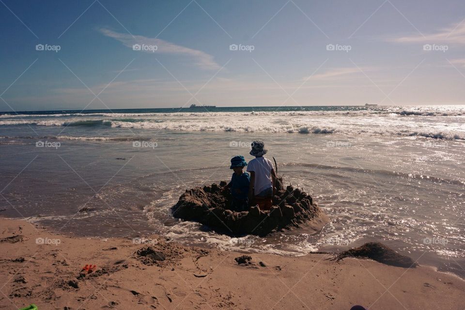 Boys in their sand fort surviving a wave