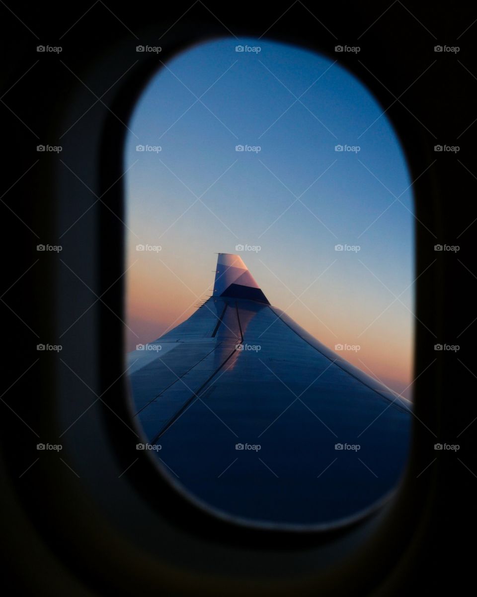 Travel. Escape away for a while. A window shot of the wing of an airplane with sunset colors in the background
