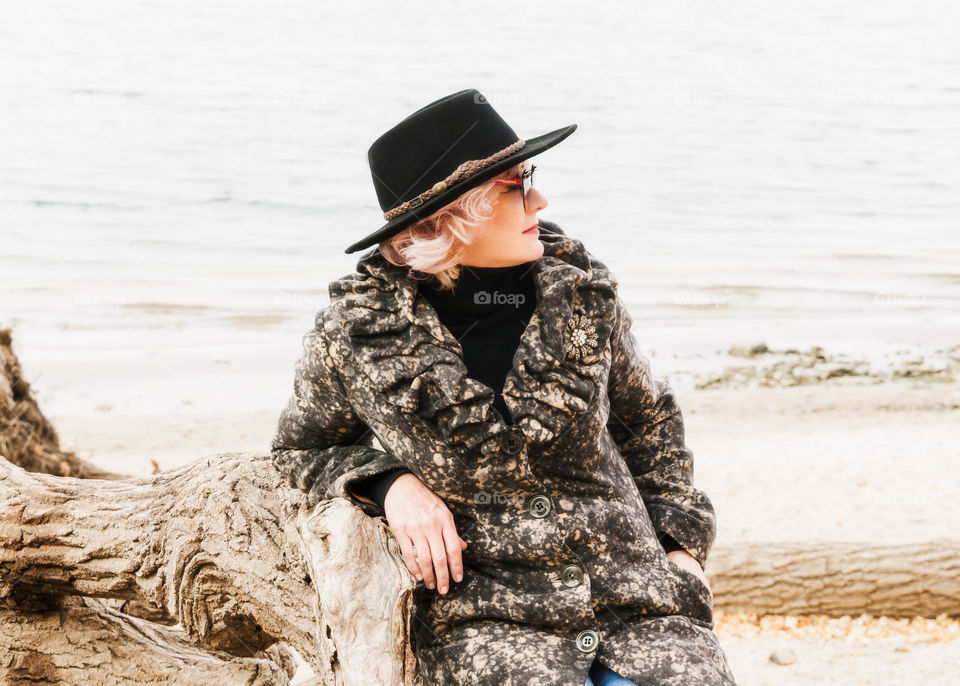 Portrait of stylish adult woman in black hat sitting next a river