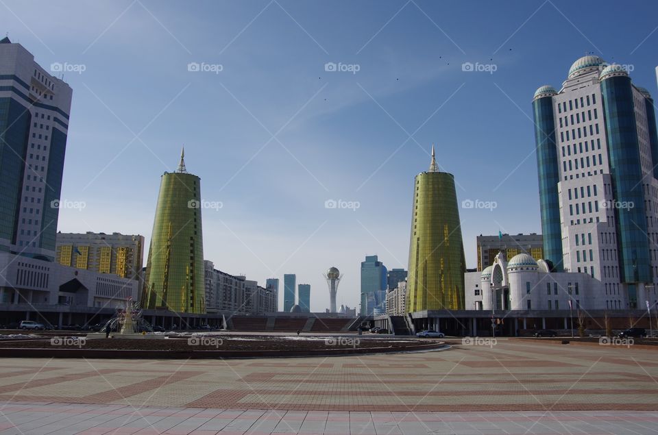 Exterior daylight.  Astana, Kazakhstan.   View from the President’s Residence.  A wide plaza, golden towers, lines receding to the Bayterek, a symbol of national pride.