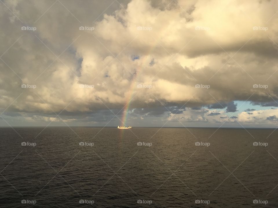 Rainbow leading to a small boat out at sea, cloudy day with some showers just beginning to clear up and give way to sun