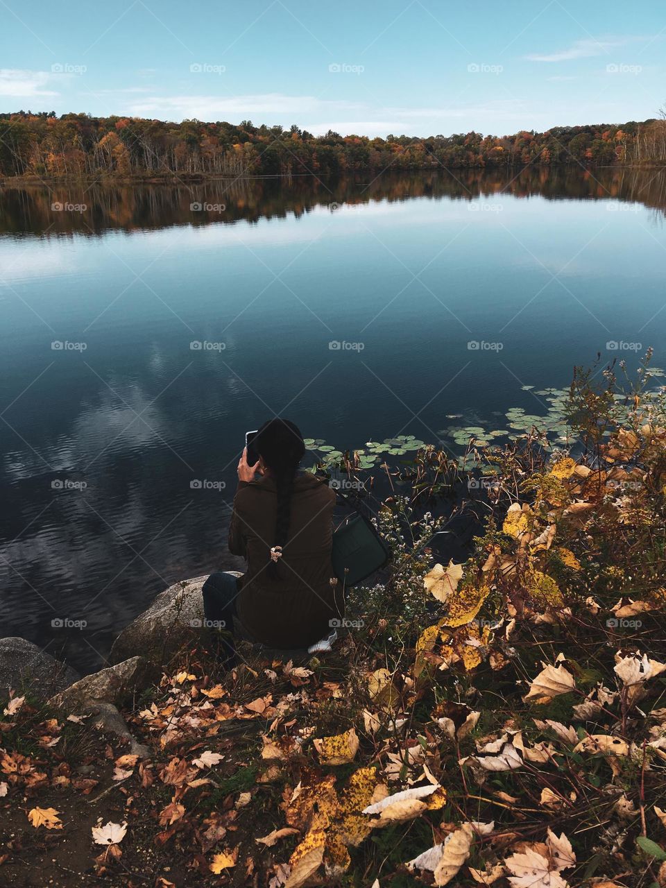 A person taking picture of fall foliage in front of a river at upstate New York. 