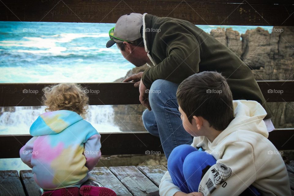 Father and children looks at the ocean through wooden barriers