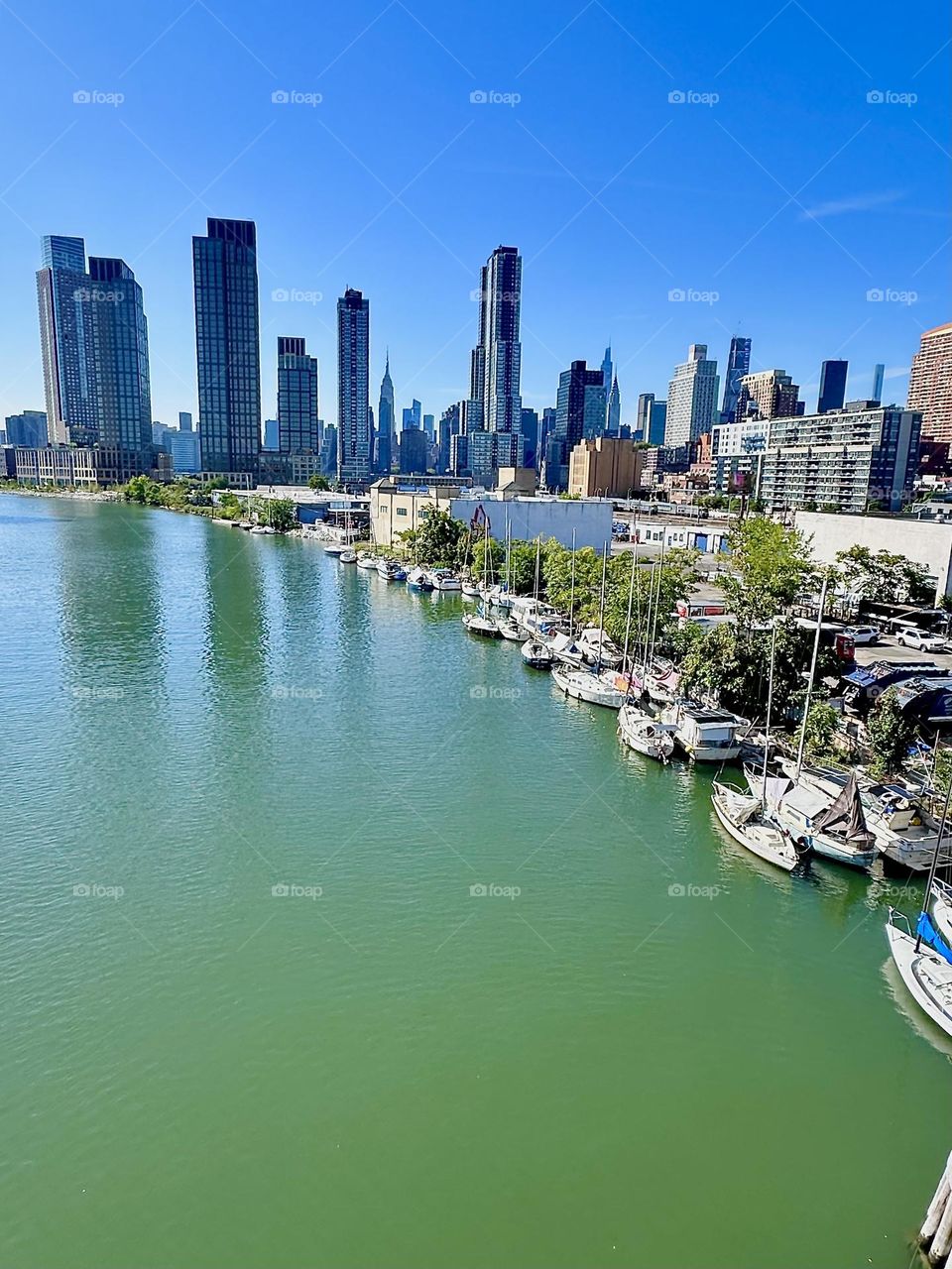 This is picturesque “Newtown Creek” with its great variety of boats seen from the “Pulaski Bridge” that connects “Greenpoint”, Bklyn to LIC, Queens. Across the water we see “Manhattan” including the “Empire State Building”. 2024. Hypnotic Productions