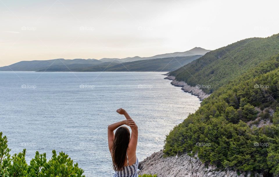 Rear view of young woman with raised arms admiring amazing sea coast