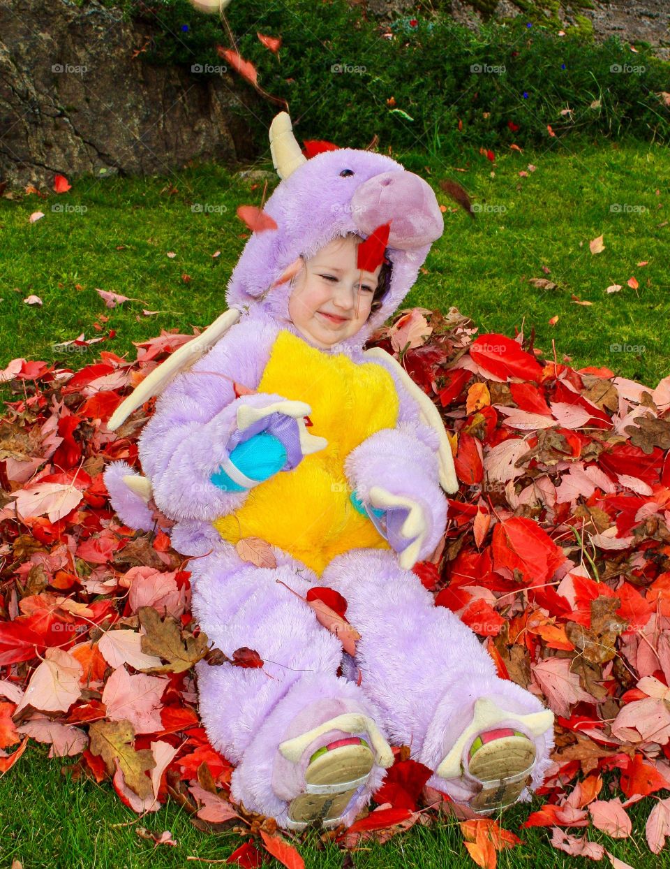 Girl dressed as purple dragon sits under falling leaves 