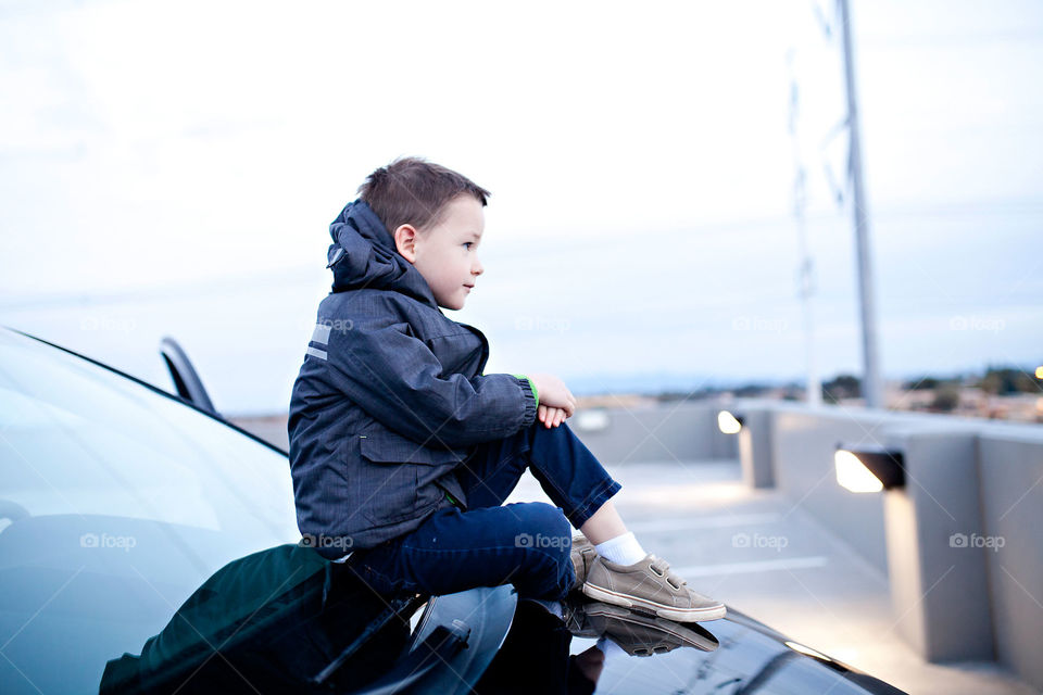 Boy sitting on hood of a car