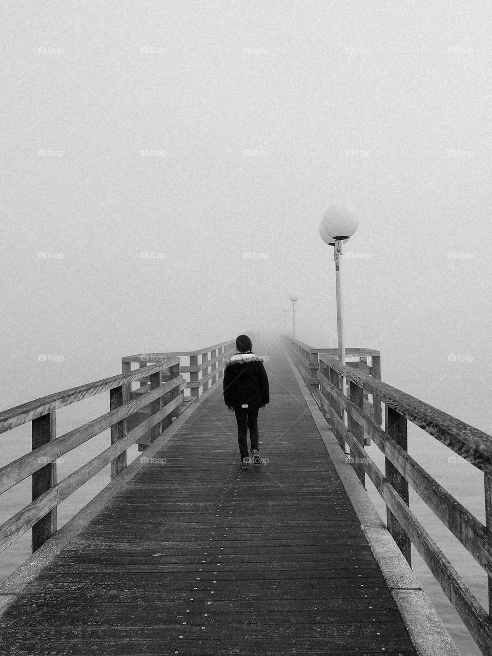 A lonely boy walking on a foggy bridge