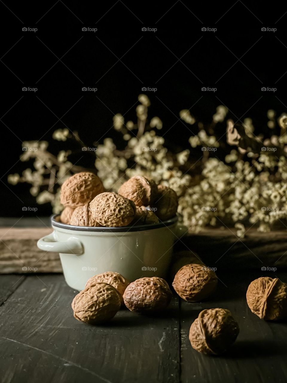 Walnuts in a ceramic bowl and some are scattered on the wooden table