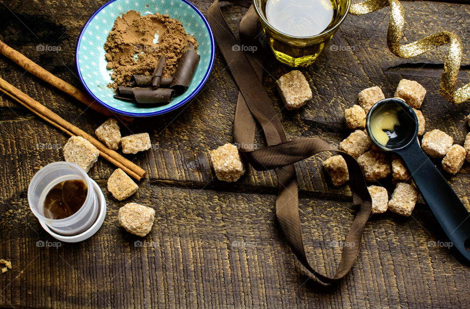 Sweet cooking and baking ingredients raw sugar, organic honey, oil, cinnamon sticks, brown sugar, chocolate, cocoa powder on rustic wood background with measuring spoons 
