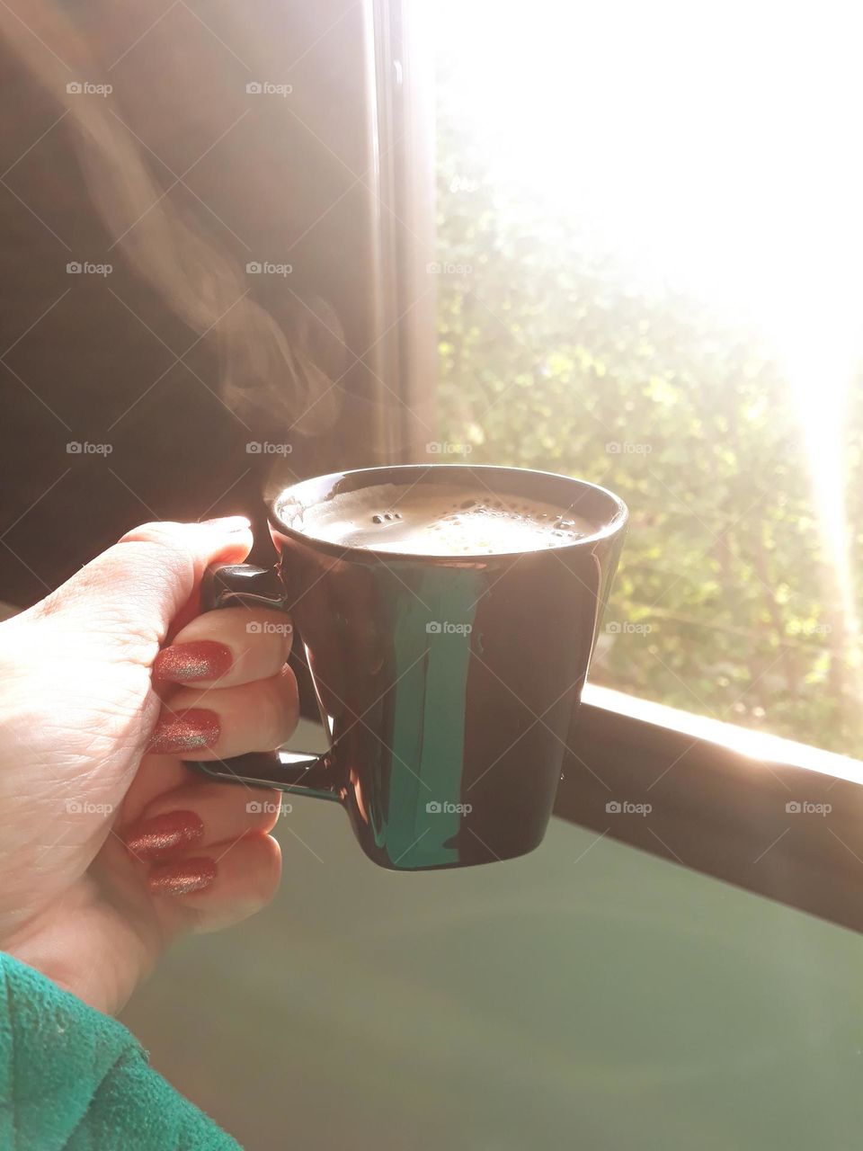 Mão feminina segurando xícara preta com café quente e cremoso.