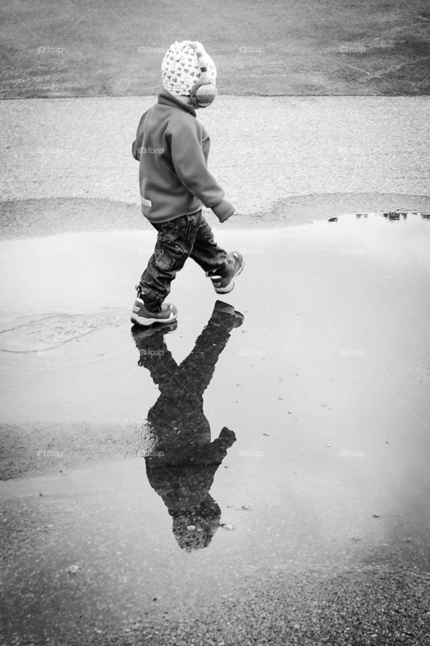 Child walking and reflection in a puddle bw