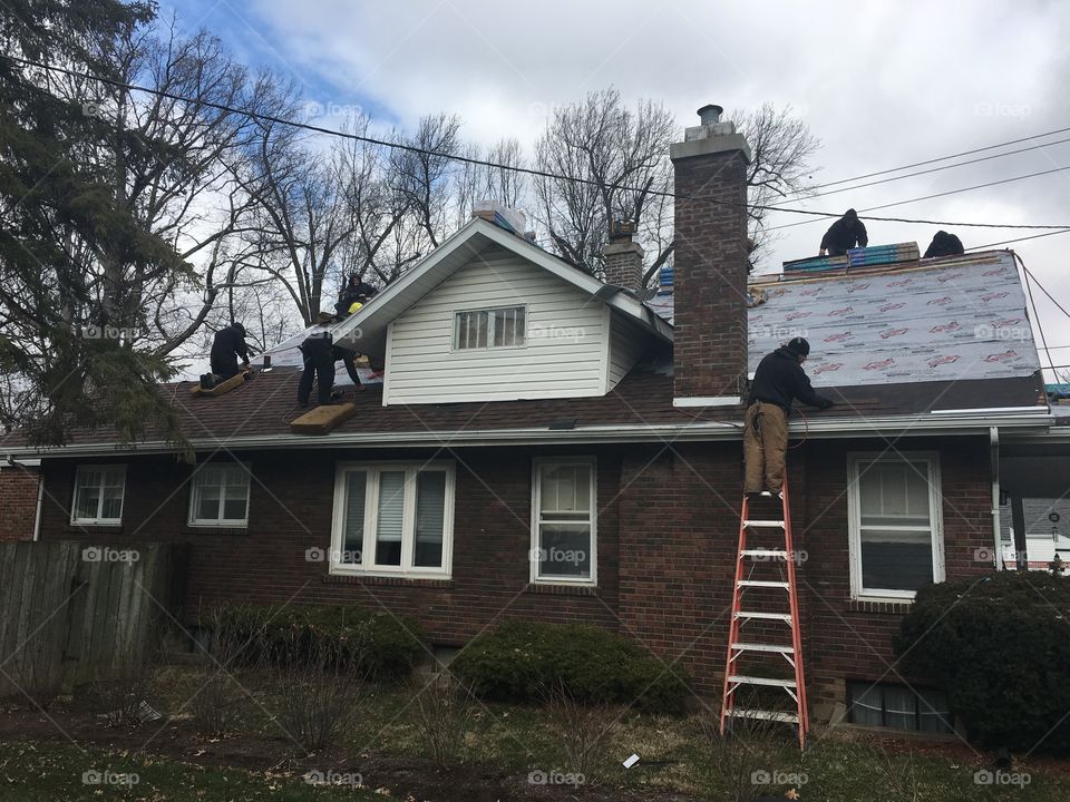 Men working on replacing the roof of our brick house with ladders and tools