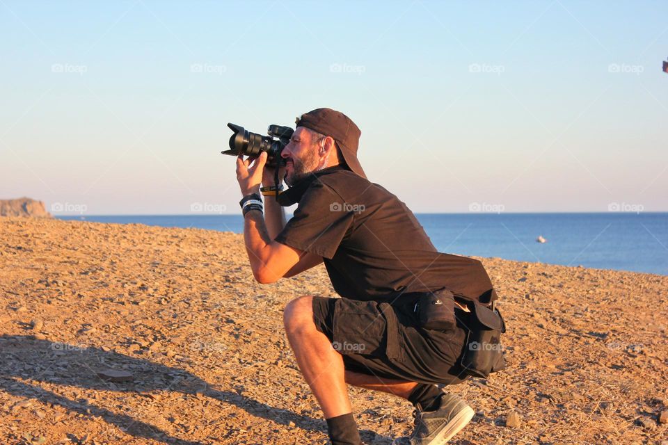 a professional photographer sat down on a jacket and takes a photo on the beach at sunset