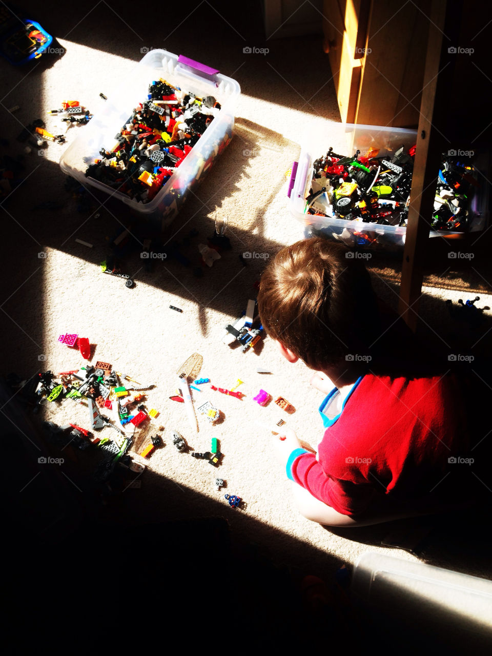 Young boy building Legos on the floor of his bedroom in a shaft of