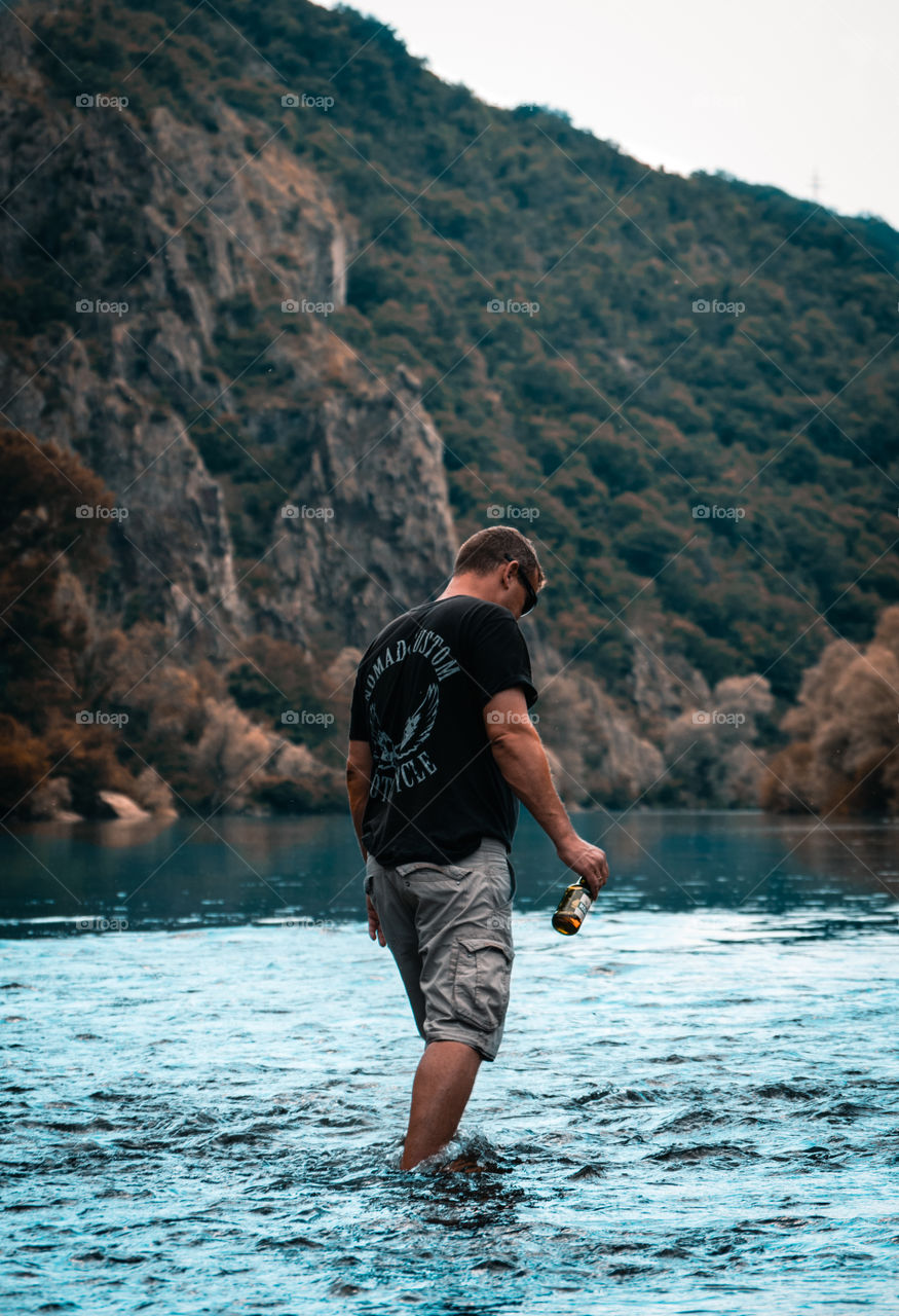 Man holding a beer at a lake.