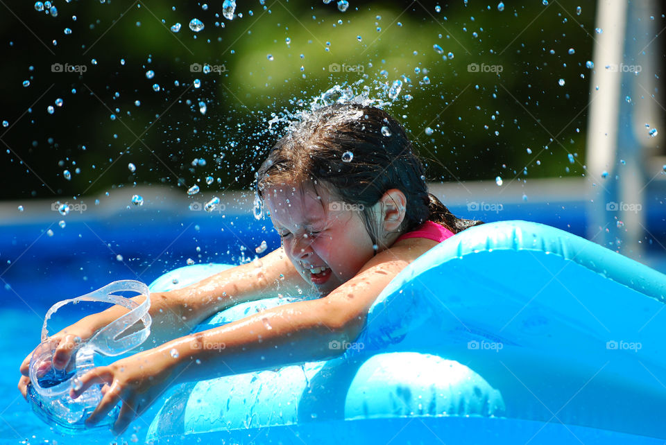 Young Girl Splashing Water in Swimming Pool on a Float