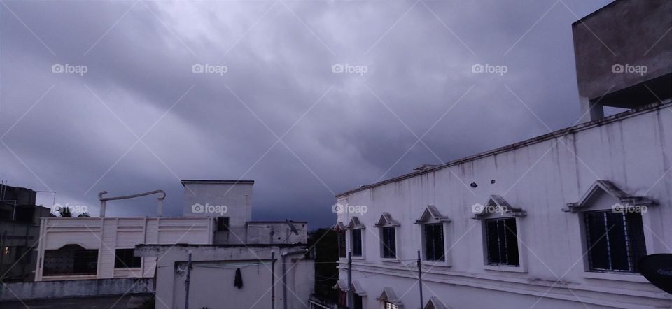 This picture was taken on a flat roof when the dark cloudy sky was shown and rain was coming. One building with rows of windows showing which are creating a beautiful scene.