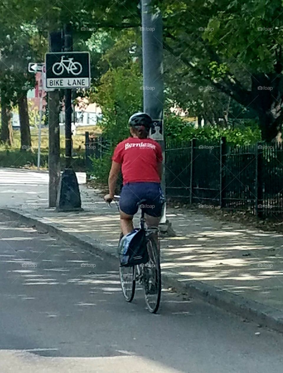 Person wearing bicycle 🚲 helmet, shorts and red shirt, easily seen. Riding in marked bike lane in street. City, urban or town unknown.
Riding bicycle in marked lane on asphalt road.