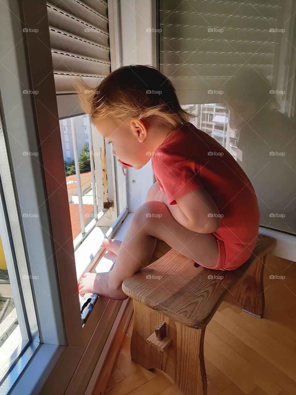 A little girl sits on a bench and watches outside