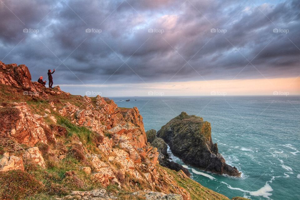 Extreme Selfie. Two pool on a cliff side overlooking an ocean at sunset take a selfie.