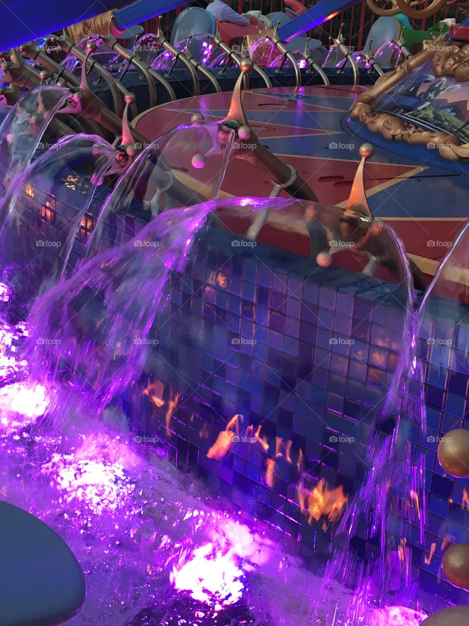 A close up of a color-changing water fountain that is lit up in purple lights. It’s taken at the Dumbo ride in Disney World at night 
