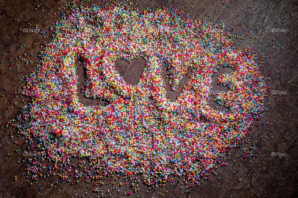 Word love written in sugar candy sprinkles. Different colors. Dark textured background. Flat lay. Heart shape