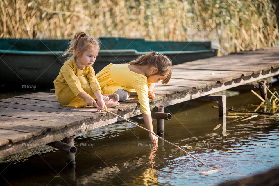 Little sisters playing near lake at autumn day 