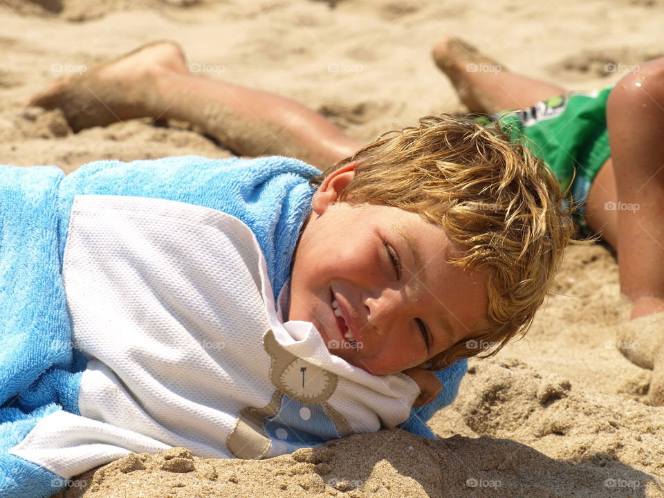 Cute boy lying on sand at beach with towel