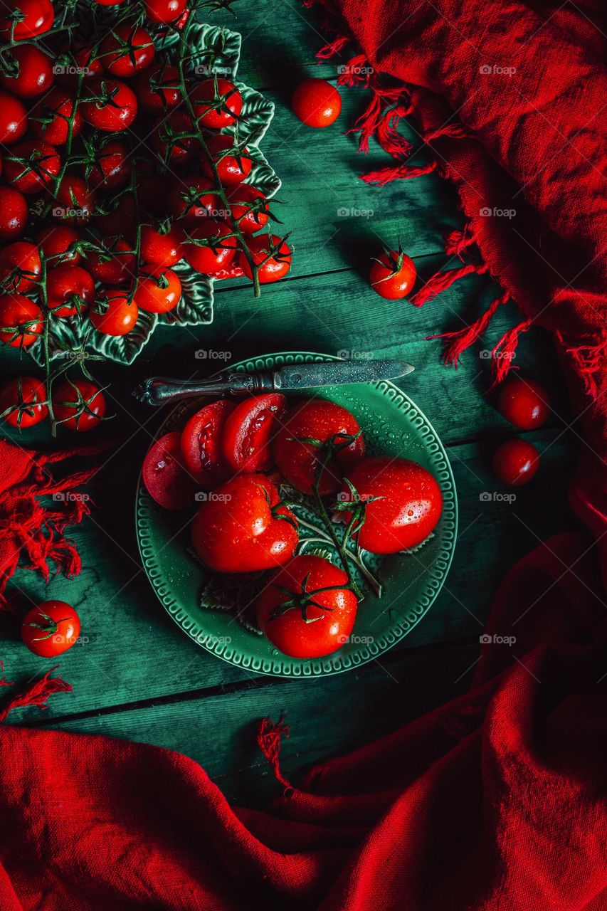 The vibrant red color of flamenco and cherry tomatoes is incredibly delicious, and they are presented on a green background with drops of water.