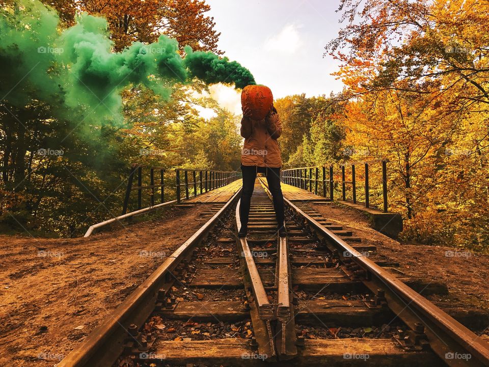 Woman holding pumpkin with green smoke at railroad track