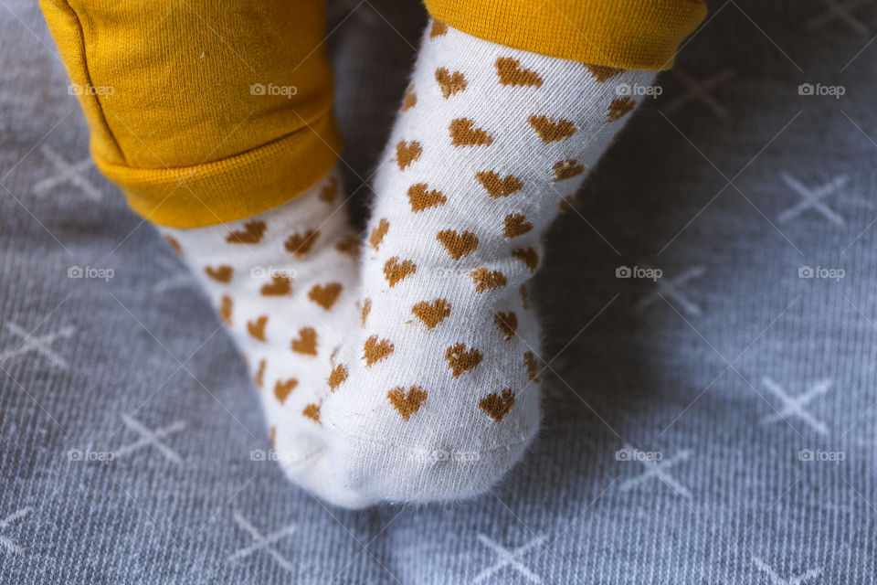A portrait of cute little baby feet and legs wearing white socks with little hearts on them.