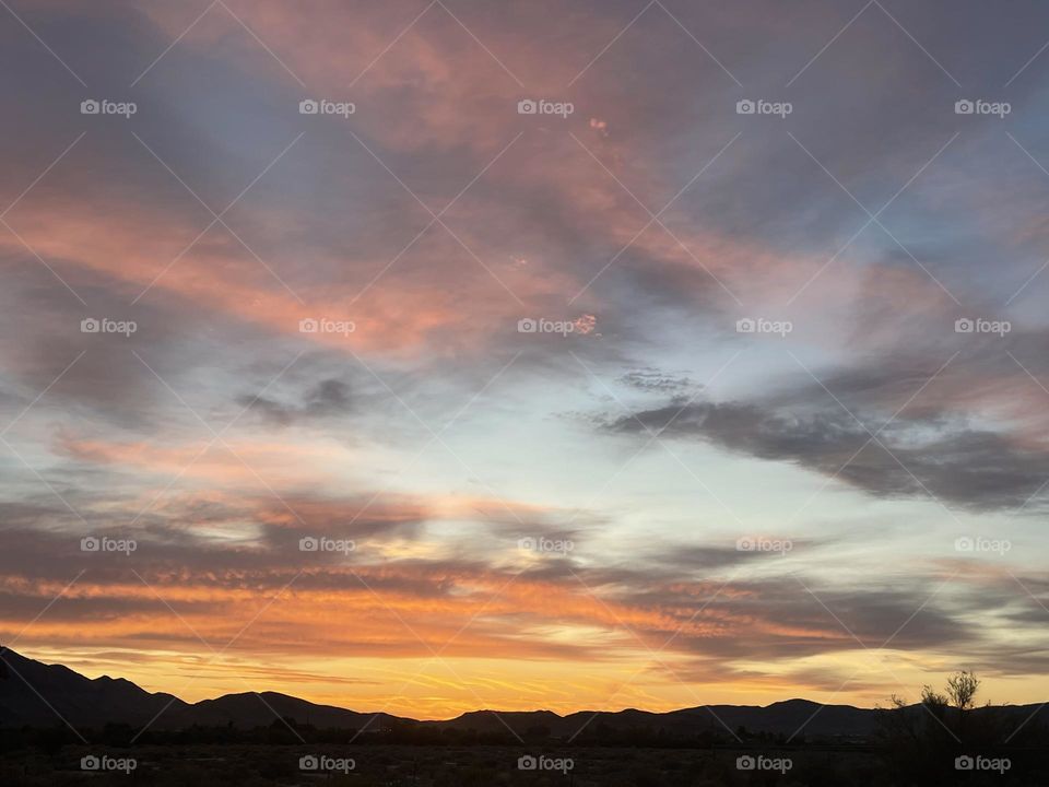 A orange and pink sunset with clouds and mountains.