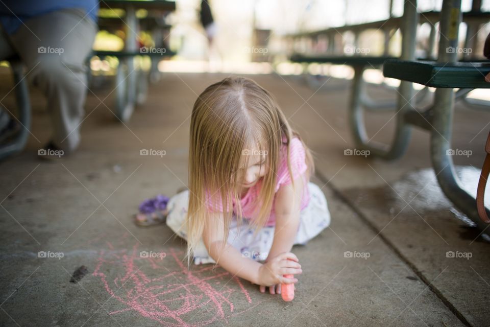 Girl drawing on concrete by picnic tables with sidewalk chalk. Young girl drawing on ground, creating pictures with chalk