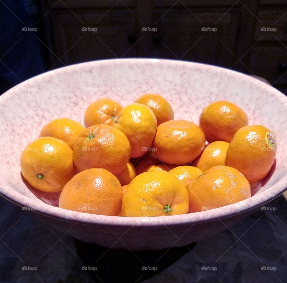 Large pink speckled bowl full of small tangerines orange color, sweet little Halos too, healthy foods.